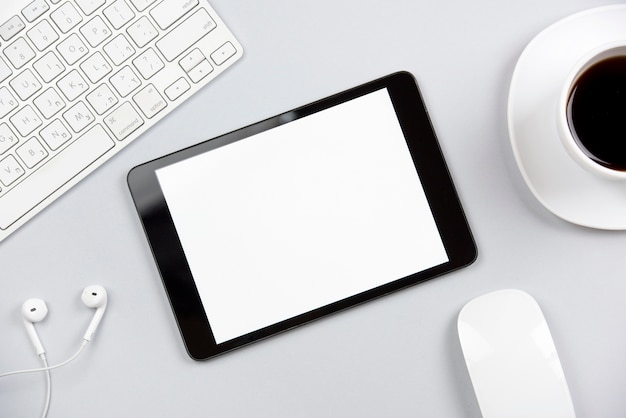 An overhead view of keyboard; earphone; mouse; digital tablet and coffee cup on gray background