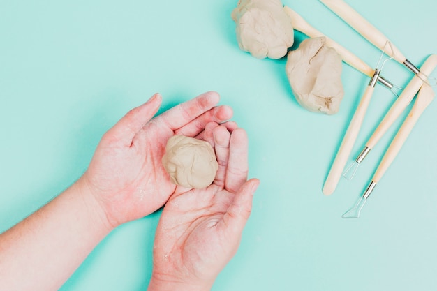 An overhead view of kneaded dough on man's hand with sculpting tools on mint green backdrop