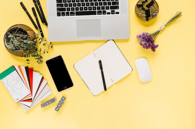 Overhead view of laptop and cellphone with stationery on yellow background