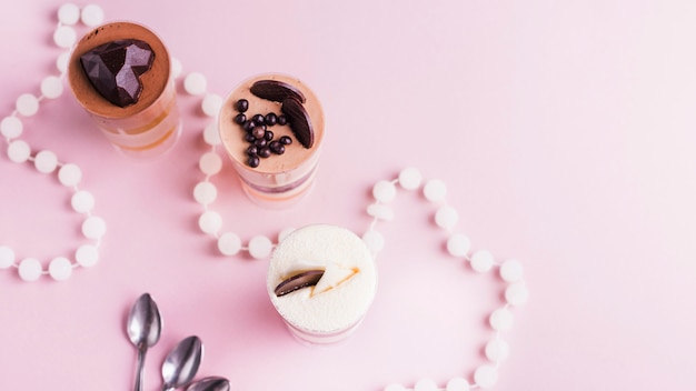 An overhead view of layered desserts with decoration on pink backdrop with necklace and spoons