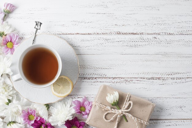 An overhead view of lemon tea cup decorated with flowers and gift box on wooden desk