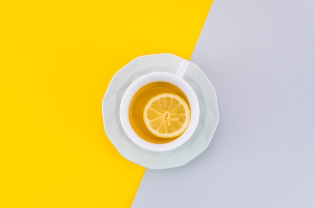 An overhead view of lemon tea cup and saucer on white and yellow background