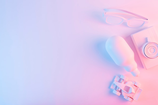 An overhead view of lightbulb; spectacles; formula one car and camera against pink backdrop with blue light