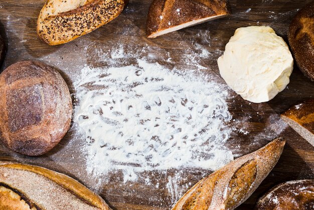 An overhead view of loaf of bread; baguette and kneaded dough with flour on wooden desk