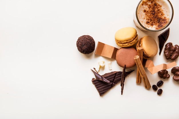 An overhead view of macaroons; chocolate ball and coffee glass on white background