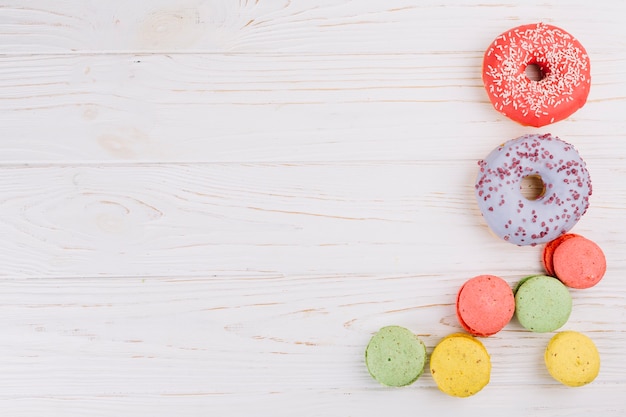 An overhead view of macaroons and donuts on wooden texture background