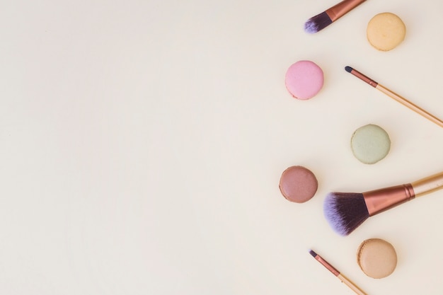 Overhead view of makeup brushes and macaroons on beige background