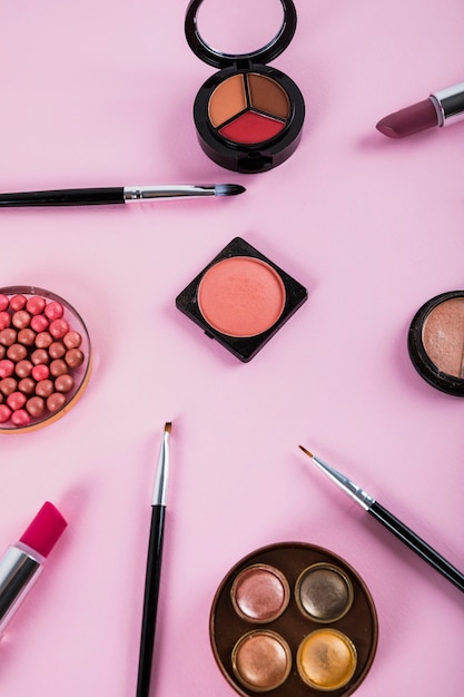 Overhead view of makeup kit with brushes on pink backdrop