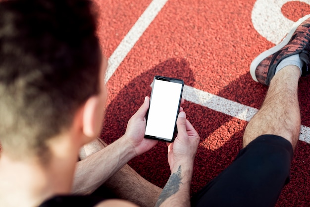 Una vista aerea dell'atleta maschio che si siede sulla pista utilizzando il telefono cellulare