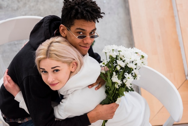 Free photo an overhead view of man holding white flower bouquet in hand embracing her girlfriend