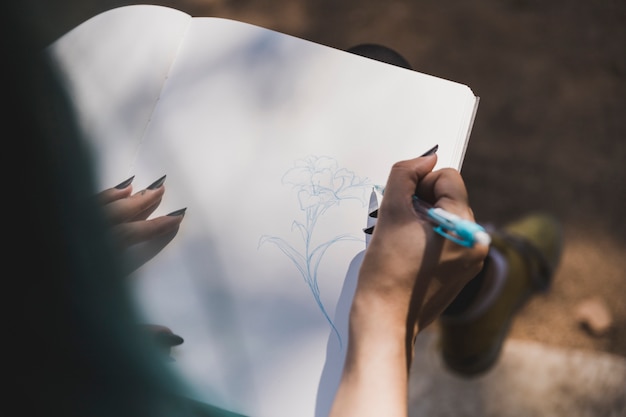 Foto gratuita una vista ambientale della mano dell'uomo che disegna fiore sul taccuino