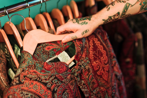 Free photo an overhead view of man with tattoo in his hand looking at clothes hanging on rail