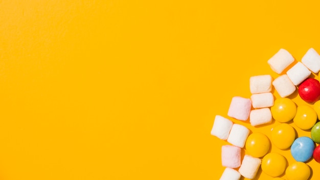 An overhead view of marshmallow and colorful candies on yellow background