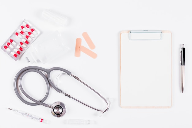 Free photo overhead view of medical equipments with paper on clipboard and pen on white backdrop