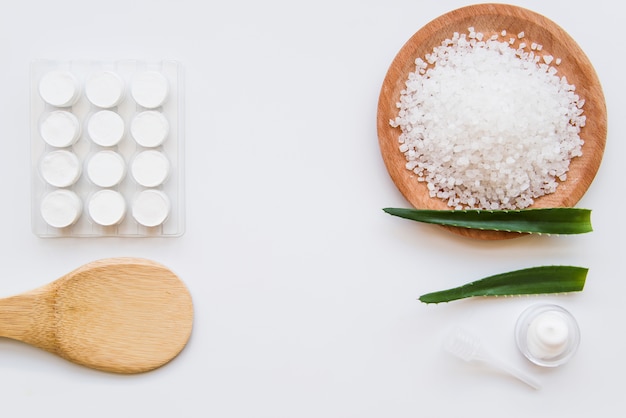 An overhead view of moisturizer cream with rock salt and aloevera leaves on white background