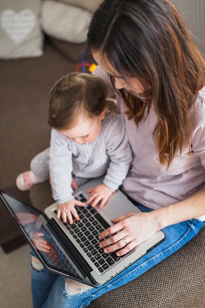 Punto di vista ambientale della madre che si siede con il suo bambino che per mezzo del computer portatile