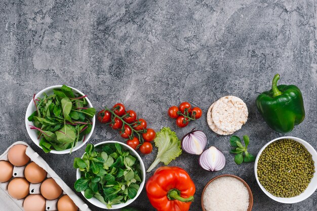 An overhead view of mung bean; eggs; spinach; vegetables; lettuce and puffed rice cake on concrete background