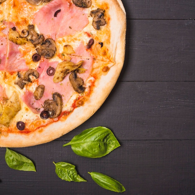 An overhead view of mushroom and meat pizza with basil leaves on wooden plank