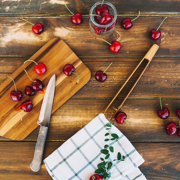 Foto gratuita vista dall'alto del tovagliolo con coltello e ciliegine rosse fresche sul tagliere di legno