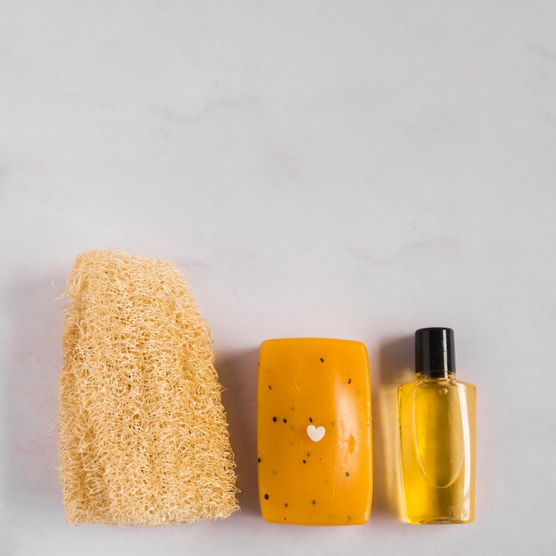 An overhead view of natural loofah; herbal soap and essential oil bottle against white background