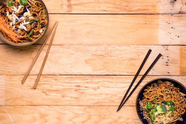 An overhead view of noodles bowls with chopsticks on wooden plank