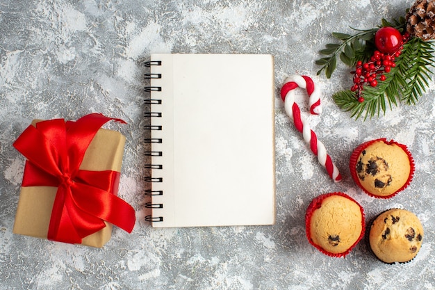 Overhead view of notebook and small cupcakes candy and fir branches decoration accessories and gift with red ribbon on ice surface