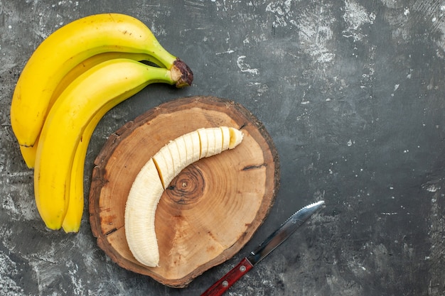 Overhead view nutrition source fresh bananas bundle and chopped on wooden cutting board knife on gray background