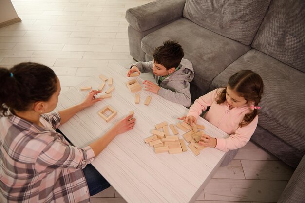 ボードゲームをしているママと子供たちの俯瞰図、木造建築物、家の居間のテーブルの上の構造物。家族の娯楽と教育的な趣味の概念