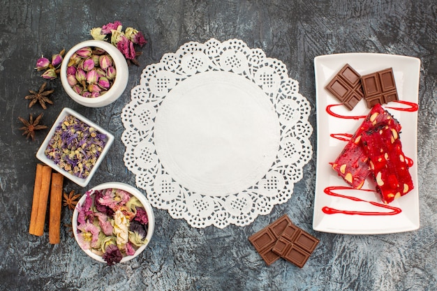 Бесплатное фото Вид сверху на шоколадные конфеты на белой тарелке, засушенные цветы и кусок кружева на серой земле