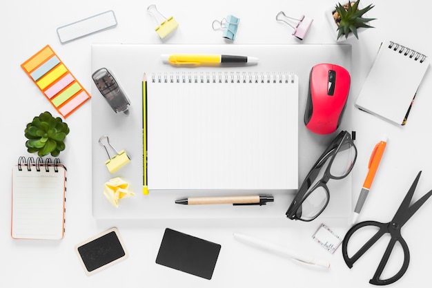 An overhead view of office stationeries on laptop over white background