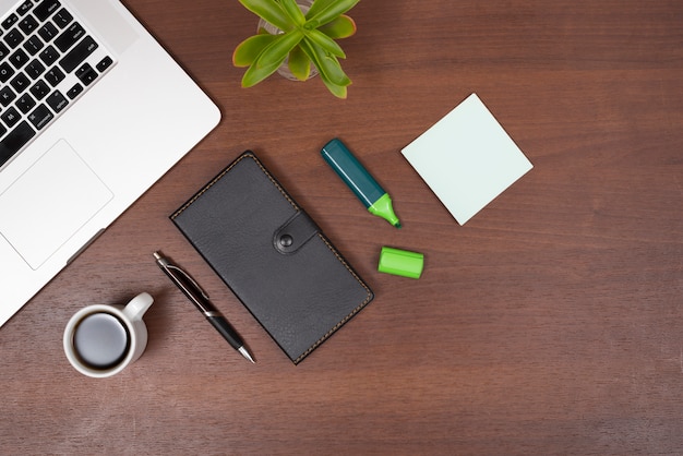 Overhead view of office supplies; tea; plant and laptop on wooden desk