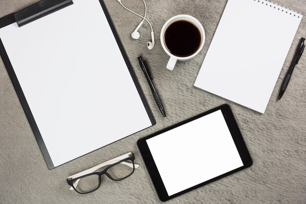 An overhead view of office supplies with coffee cup and digital tablet on gray desk