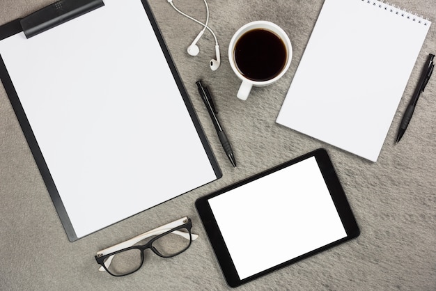 An overhead view of office supplies with coffee cup and digital tablet on gray desk