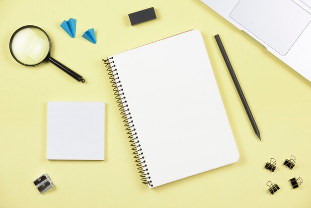 An overhead view of office supplies with laptop on yellow background