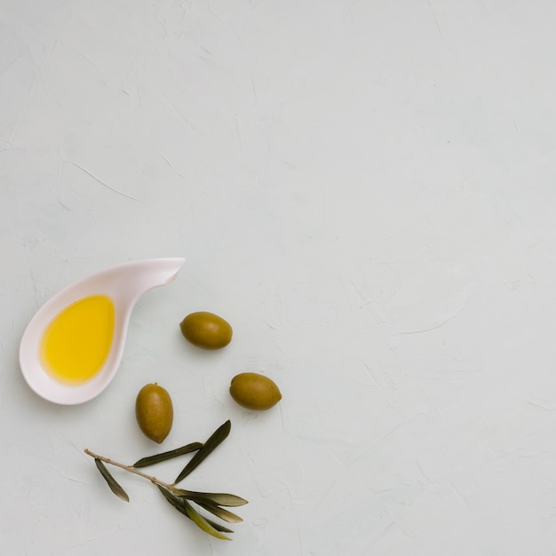 An overhead view of olive; leaves and oil on white concrete background