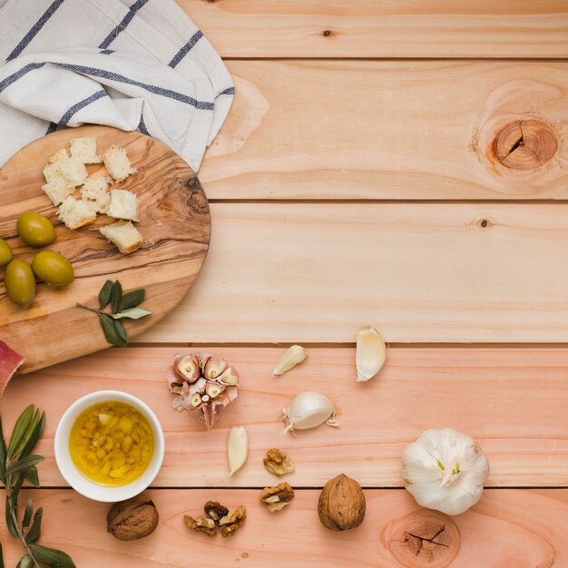 An overhead view of olives; bread; walnuts and infused olive oils on wooden table