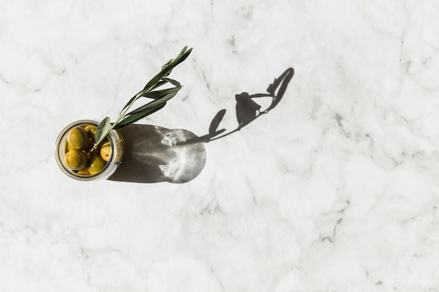 Overhead view of olives jar with twig on marble background