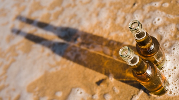 An overhead view of an open beer bottles with shadow on shallow water at beach