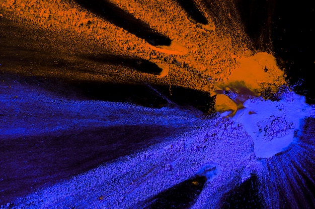 Overhead view of orange and blue powder colors splatted on dark backdrop