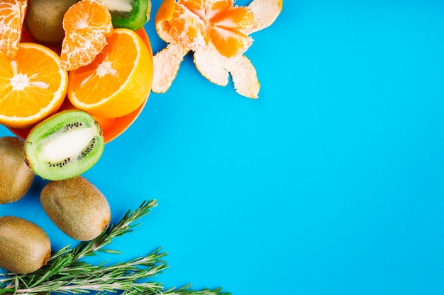 An overhead view of oranges; kiwi and rosemary on blue backdrop