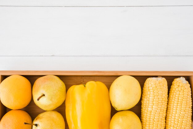 An overhead view of oranges; pears; bell pepper; lemon and corn on wooden tray over the white desk