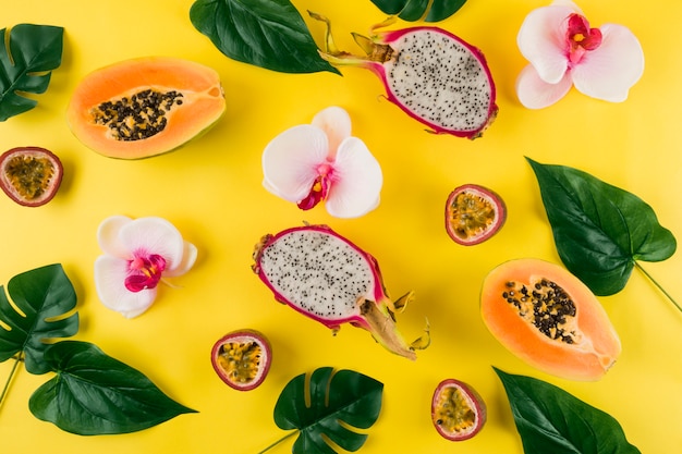 An overhead view of orchid flower; leaves; dragon fruit and papaya on yellow backdrop