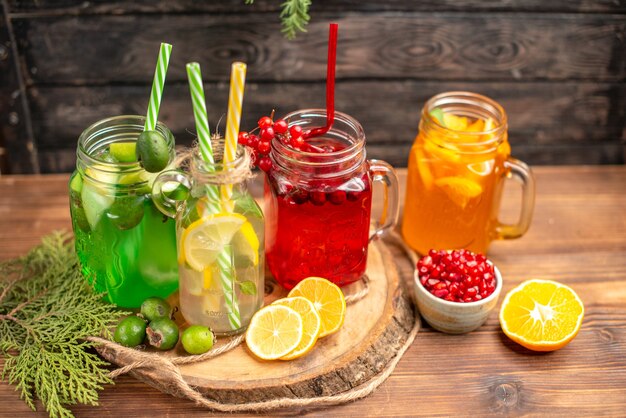 Overhead view of organic fresh juices in bottles served with tubes and fruits on a wooden cutting board on a brown table