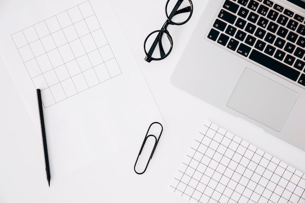 An overhead view of page; pencil; paper clip; eyeglasses and laptop on white background