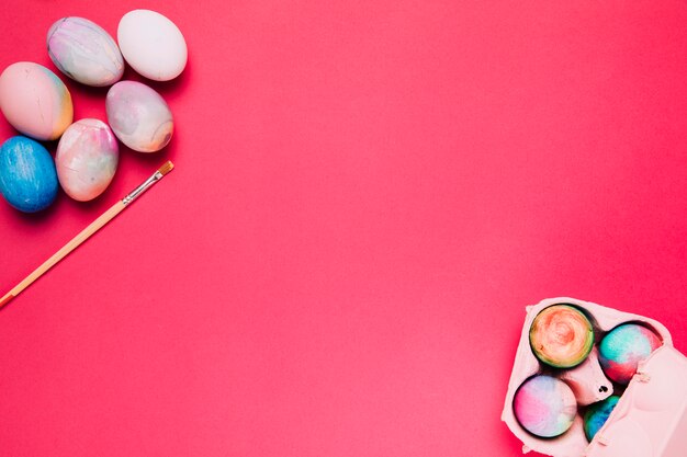 An overhead view of painted easter eggs and carton with paint brush on pink backdrop