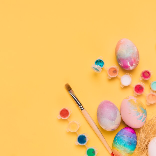 An overhead view of painted easter eggs; paint brush and water color paint on yellow backdrop