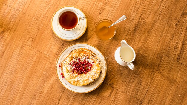 Overhead view of pancake with honey and tea cup on wooden table