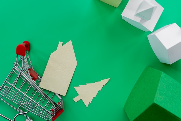 An overhead view of paper houses with shopping trolley on green background