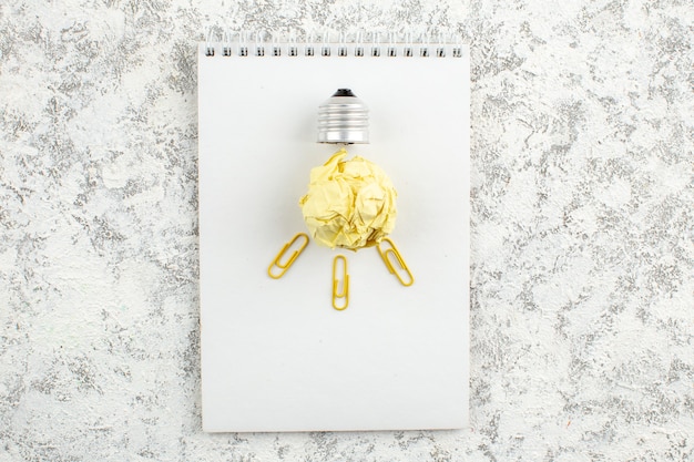 Free photo overhead view of paper light bulb on white closed spiral notebook on white surface