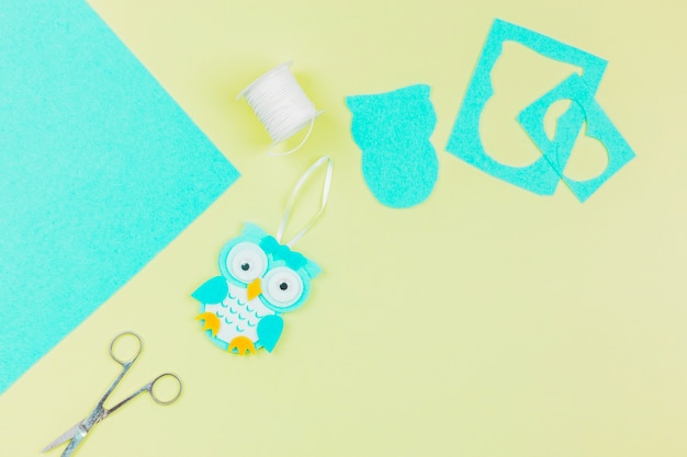 An overhead view of paper owl with thread spool and scissor on yellow background